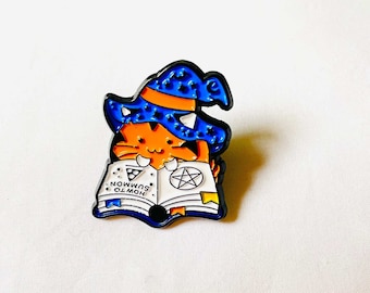 May include: A blue and orange enamel pin of a cat wearing a witch's hat and reading a book that says "How to Summon Ol' Moh".