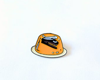 Könnte beinhalten: Eine gelbe Emaille-Anstecknadel mit einer Heftmaschine in einer Schüssel mit orangefarbenem Wackelpudding auf einem weißen Teller.