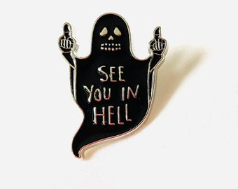 May include: Black enamel pin featuring a ghost with a skull face giving the middle finger and the text "See you in hell".