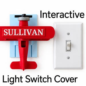 May include: A red airplane-shaped light switch cover featuring the name SULLIVAN in white letters on the wing. The airplane is mounted on a light blue rectangular base next to a standard white toggle light switch plate with the text Interactive.