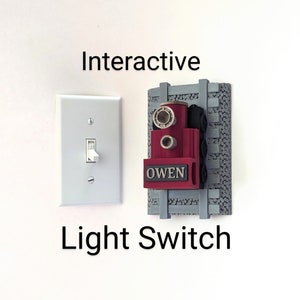 Peut inclure: Un interrupteur interactif avec le nom "OWEN" sur un design rouge et noir sur le thème du train, monté sur une voie grise. À côté, un interrupteur blanc standard. Les mots "Interactive Light Switch" sont écrits en noir.