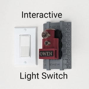 May include: An interactive light switch with the text "Interactive Light Switch". The switch features a red train design with the name "OWEN" on the front. The switch is mounted on a gray track design.