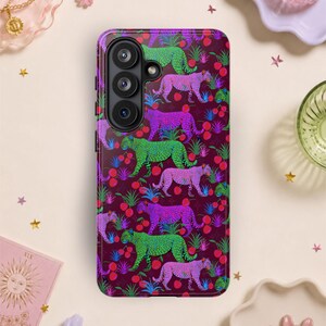 May include: A phone case with a repeating pattern of colorful cheetahs and red berries on a dark burgundy background. The cheetahs are in shades of green, purple, and pink. The case has a camera module on the upper left.