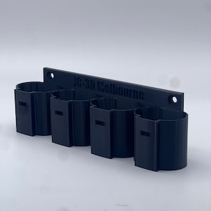 May include: A black 3D-printed wall-mounted organiser with four cylindrical compartments. The organiser has a rectangular backplate with the text "10-3D Melbourne" and two mounting holes. The compartments have rectangular cutouts.