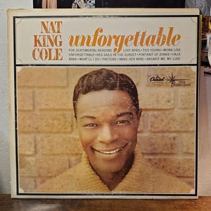 May include: A square vinyl record cover featuring a portrait of Nat King Cole wearing a tan sweater against a brick wall. The text reads Nat King Cole, Unforgettable, and lists song titles including Mona Lisa and Too Young. Capitol Records logo.