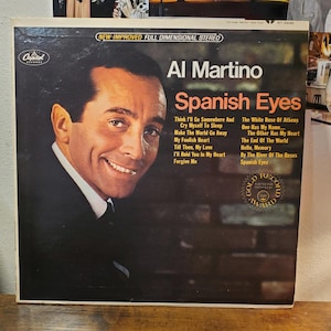 May include: A vintage vinyl record album cover featuring a portrait of Al Martino on the left and the title Spanish Eyes in orange text on the right. The cover includes a tracklist, the Capitol Records logo, and a gold record award seal.