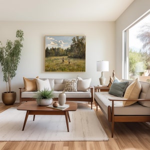 May include: A living room with a beige sofa and a matching loveseat, both with throw pillows. A wooden coffee table sits in front of the sofa. A painting of two children walking in a field hangs on the wall above the sofa. A potted plant sits on the floor next to the sofa.