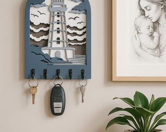 Könnte beinhalten: Ein blauer, bogenförmiger Wand-Schlüsselhalter mit einem geschichteten, lasergeschnittenen Design aus Leuchtturm, Wolken und Vögeln. Das Stück verfügt über fünf schwarze Metallhaken, an denen drei Schlüsselbunde hängen.