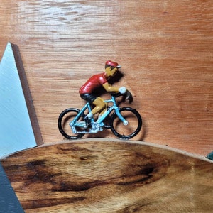 Retro vintage cyclist riding through a stylised wooden plaque wall art depicting mountains and hills, a Tour de France tribute