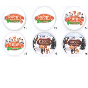 May include: A collection of six white circular buttons featuring the text "RUDOLPH RED-NOSED REINDEER THE MUSICAL" in various designs. Some buttons include illustrations of characters from the musical, such as Rudolph, Santa, and elves. The buttons are numbered from 1 to 6.