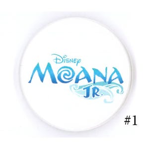 May include: A white, circular button featuring the Disney Moana Jr. logo in shades of blue. The text "#1" is in black on the lower right side of the button.