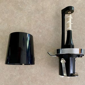 May include: A black food processor with a white auger and a detached black plastic cover. The food processor has a silver metal band and a black handle. The auger is white and has a spiral design.