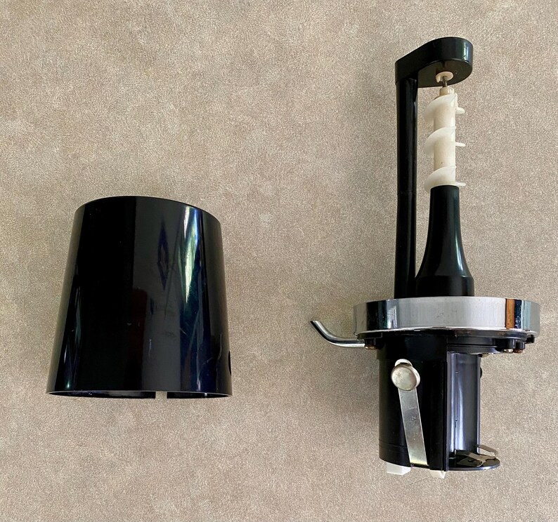 May include: A black food processor with a white auger and a detached black plastic cover. The food processor has a silver metal band and a black handle. The auger is white and has a spiral design.