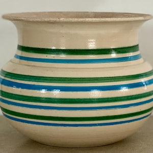 May include: A white ceramic pot with blue and green stripes. The pot is round and has a wide opening.
