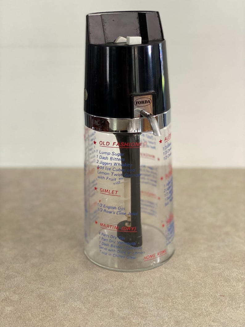 May include: Vintage cocktail shaker with a black top and a clear glass body. The shaker has a silver band and a spout. The glass is printed with cocktail recipes, including "Old Fashioned" and "Gimlet". The brand name "FORDA" is visible.