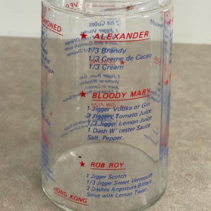 May include: Clear glass cocktail mixing jar with red and blue printed recipes for Alexander, Bloody Mary, and Rob Roy cocktails. The jar includes measurements in jiggers and dashes.