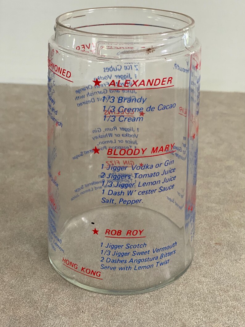 May include: Clear glass cocktail mixing jar with red and blue printed recipes for Alexander, Bloody Mary, and Rob Roy cocktails. The jar includes measurements in jiggers and dashes.