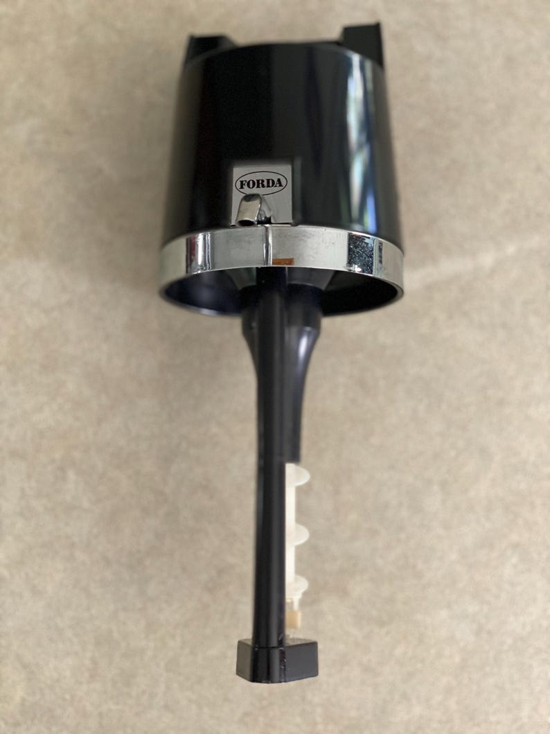 May include: A black and silver bar tool with the word "FORDA" on the front. The tool has a cylindrical top, a silver band, and a long, black stem with a white plastic piece. The base is a black, hexagonal shape.