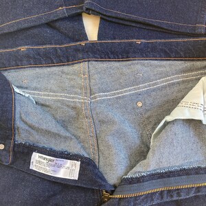 May include: Dark blue denim jeans with a zipper fly and a visible label. The jeans have a classic five-pocket design and are made of a durable denim fabric. The stitching is a contrasting orange color.