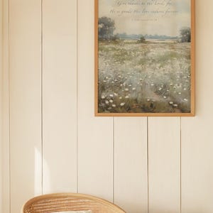 May include: A framed landscape art print with a wooden frame. The artwork depicts a field of white flowers under a soft, cloudy sky. The text "Give thanks to the Lord, for He is good; His love endures forever" is written at the top.