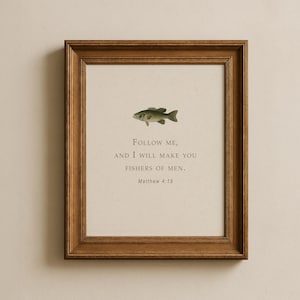 Könnte beinhalten: Ein gerahmtes Wandbild mit einer kleinen Fischillustration über dem Text "Follow me, and I will make you fishers of men. Matthew 4:19", der in einer dunklen Serifenschrift auf einem hellen cremefarbenen Hintergrund in einem braunen Holzrahmen steht.