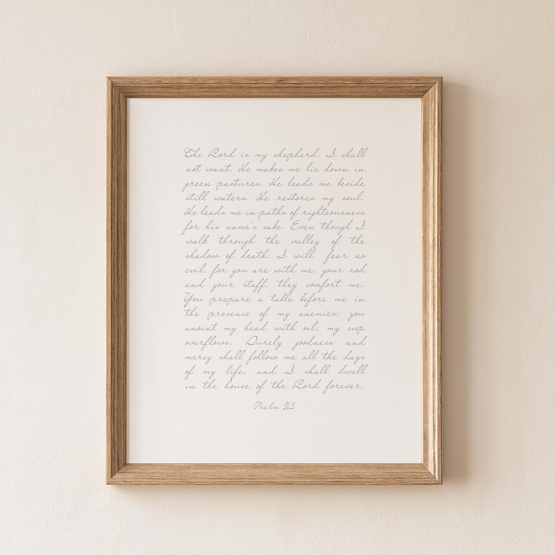 May include: A framed wall art print featuring the text of Psalm 23 written in a delicate, light gray cursive script on a white background. The frame is made of light-toned wood with a simple, clean profile, surrounding the white mat and print.