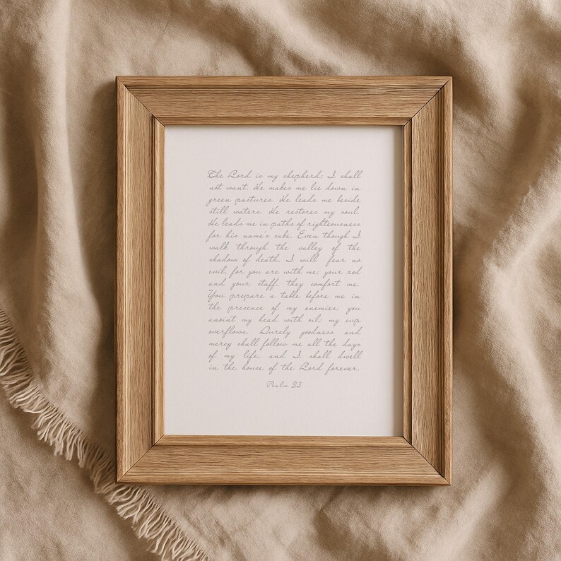 May include: A rectangular wooden frame with a light brown grain finish containing a white print featuring the text of Psalm 23 in a grey cursive script. The frame has a simple, clean design with mitered corners and a flat, smooth surface profile.