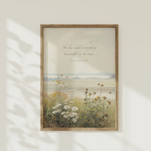 Puede incluir: Una impresión enmarcada con una pintura de acuarela de un campo de flores silvestres. La cita "Él ha hecho todo hermoso en su tiempo. Eclesiastés 3:11" está impresa en la parte superior central de la impresión.
