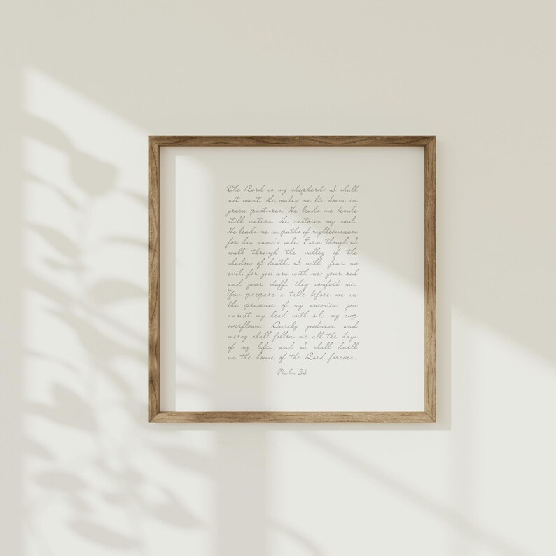 May include: A square wall art piece featuring a wooden frame and a white background with Psalm 23 written in dark grey cursive script. The text reads: The Lord is my shepherd; I shall not want. He makes me lie down in green pastures.