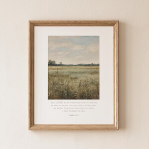May include: A framed wall art print featuring a landscape painting of a grassy field under a cloudy sky. Below the artwork, the text reads: The LORD is my strength and my shield; in him my heart trusts, and I am helped; my heart exults, and with my song I give thanks to him. Psalm 28:7.