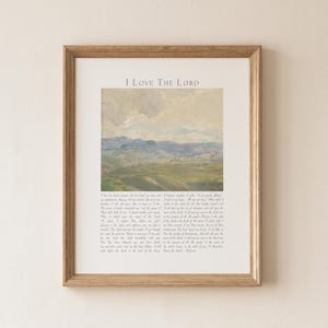 May include: Framed print with the text "I Love The Lord" above a landscape painting. The painting depicts rolling green hills under a cloudy sky. The frame is a light brown color.
