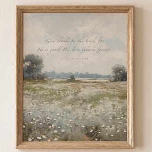 May include: A framed print featuring a pastoral landscape with a field of white flowers, trees, and a soft blue sky. The artwork includes the text "Give thanks to the Lord, for He is good; His love endures forever." from 1 Chronicles 16:34.