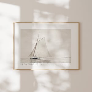 May include: A framed print featuring a watercolor painting of a sailboat on the water. The artwork is in neutral tones with the text "PROVERBS 23:24" and a Bible verse. The frame is gold.