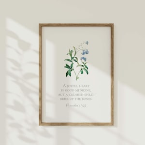 Könnte beinhalten: Ein gerahmter Druck mit einer botanischen Illustration von blauen Blumen und grünen Blättern. Der Druck zeigt das Zitat "Ein fröhliches Herz ist eine gute Medizin, aber ein zerbrochener Geist trocknet die Knochen aus." und den Schriftvers "Sprüche 17:22".