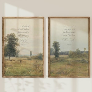 May include: Two framed landscape prints with inspirational quotes. The artwork features a pastoral scene with trees, fields, and a muted color palette. The frames are a warm, natural wood tone. The text includes the phrases "I am the light of the world" and "A new commandment I give to you."