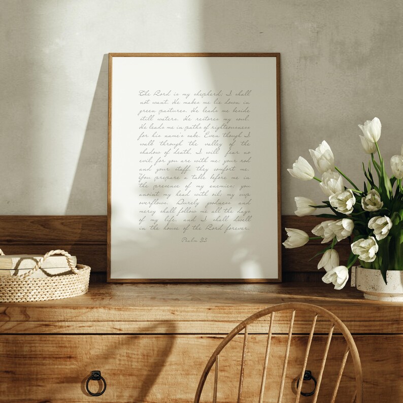 May include: A rectangular framed wall art print featuring the text of Psalm 23 in a cursive script font on a cream background. The print is displayed on a wooden surface next to a woven basket and a vase filled with white tulip flowers.