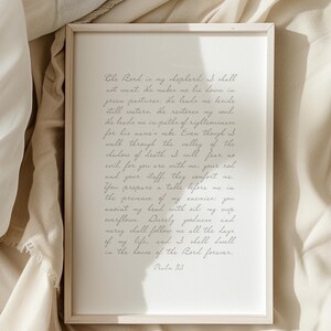 May include: A rectangular framed print featuring the text of Psalm 23 written in a cursive script. The frame is light-colored wood, and the paper is white with dark grey lettering. The text begins with The Lord is my shepherd and ends with Psalm 23.