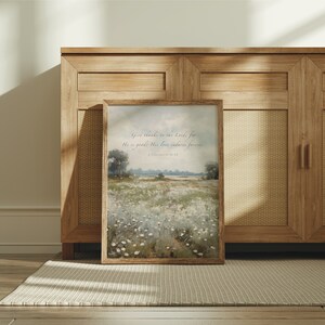 May include: A framed landscape art print with a wooden frame. The artwork depicts a field of white flowers under a cloudy sky. The text "Give thanks to the Lord, for He is good; His love endures forever. 1 Chronicles 16:34" is printed at the top.