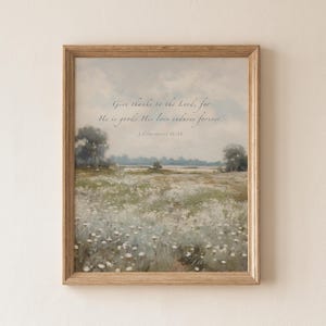 May include: A framed print featuring a pastoral landscape with a field of white flowers under a soft blue sky. The artwork includes the text "Give thanks to the Lord, for He is good; His love endures forever. 1 Chronicles 16:34."