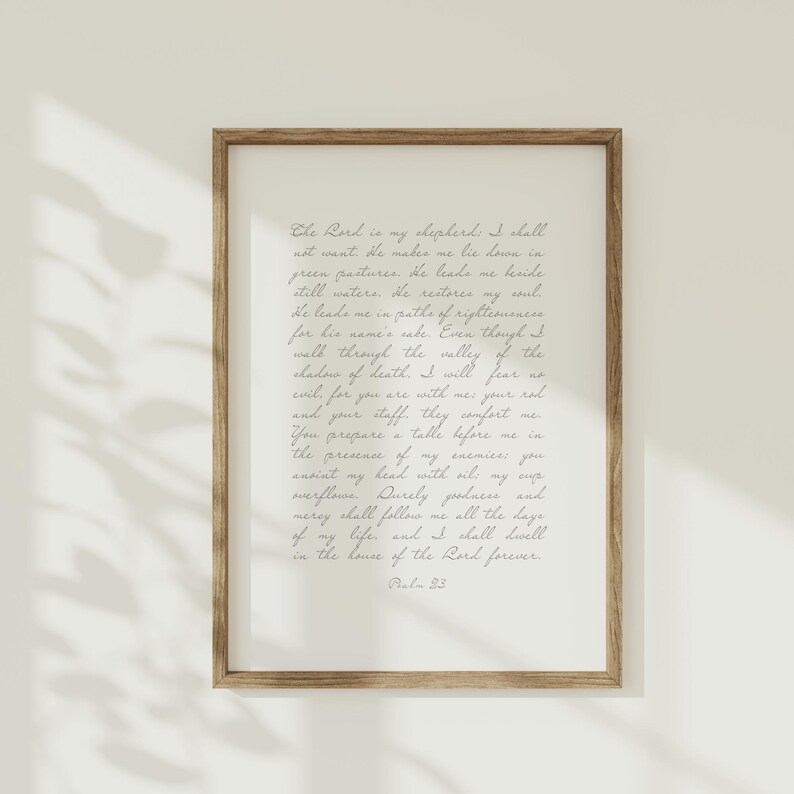 May include: A framed wall art print featuring Psalm 23 written in a dark gray cursive script on a light cream background. The text begins with The Lord is my shepherd and concludes with Psalm 23. The frame is made of medium-toned brown wood.