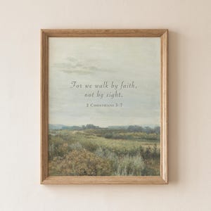 May include: A framed print with a landscape scene in soft greens, blues, and beige. The artwork displays the text "For we walk by faith, not by sight. 2 CORINTHIANS 5:7" in a graceful font. The frame is a light brown colour.