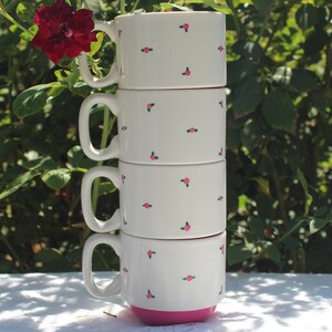 May include: A stack of four white ceramic mugs with a pink floral pattern. The mugs are stacked on top of each other, with the top mug having a pink base.