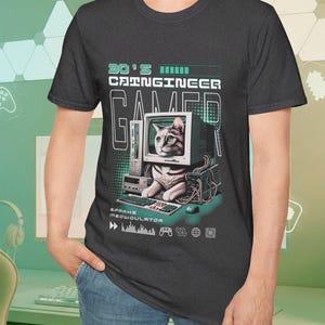 May include: Dark grey t-shirt with a graphic of a cat inside a computer monitor, keyboard, and mouse. Text reads "90's CAINGINEER GAMER" and "SPARKS MEOWOULATOR". The design has a retro, pixelated aesthetic.