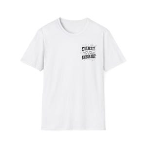 May include: White t-shirt with a crew neck and short sleeves. The shirt features a black graphic on the upper left chest that reads "I'm a little crazy but the world's insane."