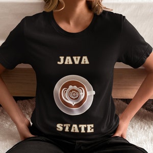 Op de afbeelding: Zwart T-shirt met de tekst "JAVA STATE" in een vintage lettertype. Een koffiemok met een hartvormig ontwerp is gecentreerd op het shirt.