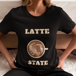 May include: Black t-shirt with the text "LATTE STATE" in a gold font. A brown coffee cup with latte art is between the words.
