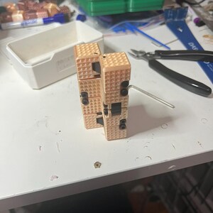 Puede incluir: Dos juguetes fidget cúbicos de color beige con una superficie texturizada y detalles negros. Una pequeña llave hexagonal está insertada en uno de los juguetes. Los juguetes están sobre una superficie blanca, con otros objetos en el fondo.