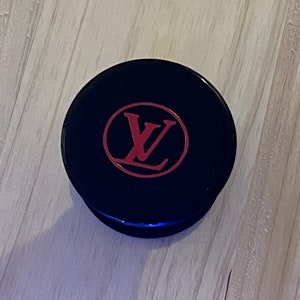 以下が含まれることがあります： 赤いLVロゴが円形に描かれた黒い携帯電話グリップ