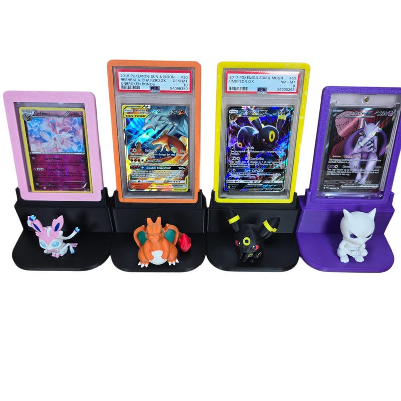 May include: Four Pokemon card display stands in pink, orange, yellow, and purple. Each stand holds a graded Pokemon card and a corresponding figurine. The cards are from the Pokemon Sun & Moon series.