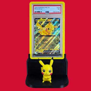 May include: A yellow Pikachu figurine stands in front of a graded Pok&eacute;mon card. The card is in a yellow holder and features a Pikachu ex card with the text "2025 POKEMON PRE EN PIKACHU ex". The background is red.